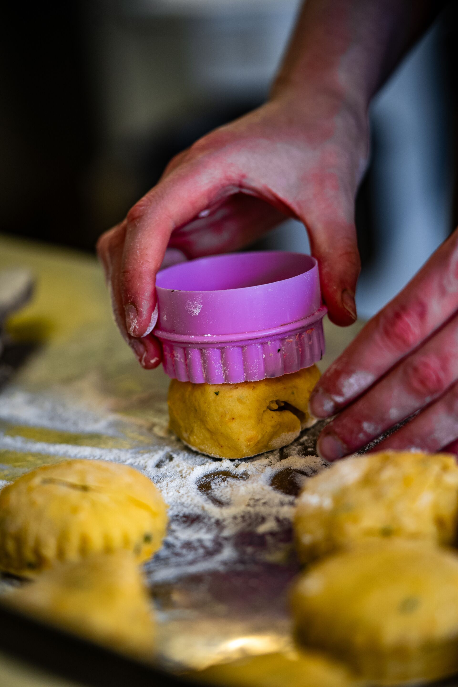 A person handling dough with a purple mold on a floured surface.