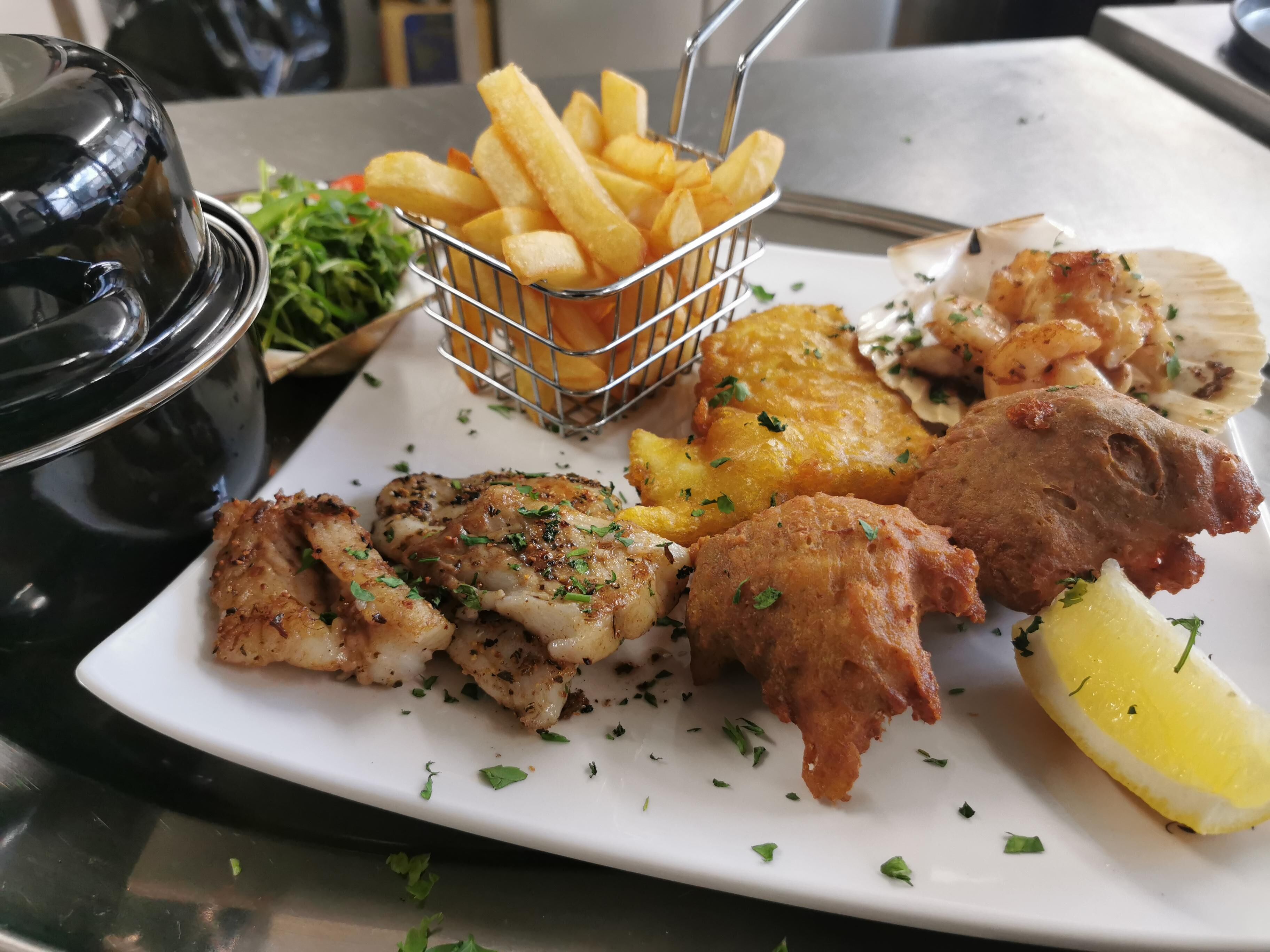 A plate of food including fish, fries, and lemon.