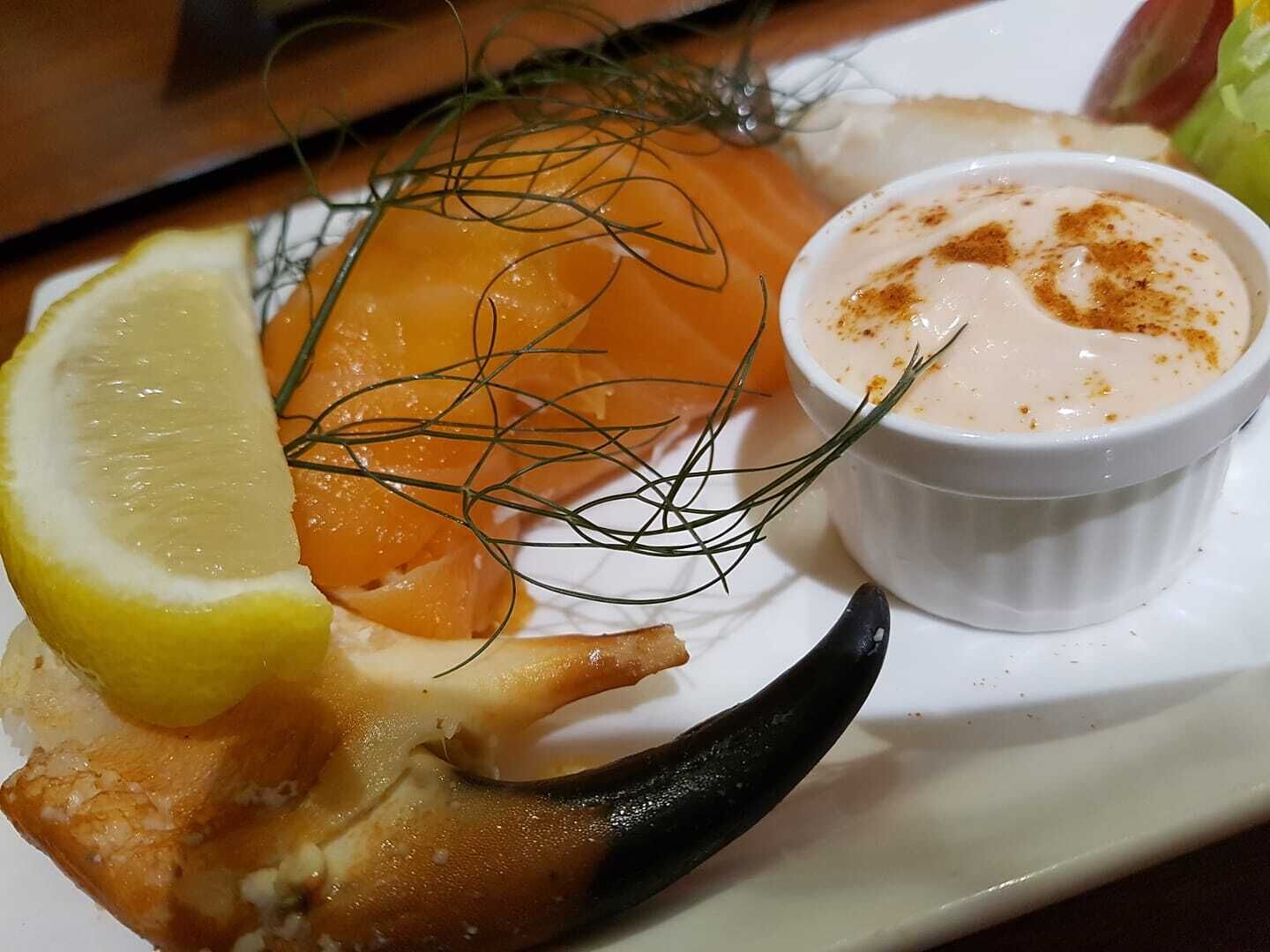 En tallrik med lax, en klyfta citron, en liten skål med sås och en bit bröd.