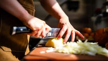 Una persona picando verduras con un cuchillo sobre una tabla de cortar.