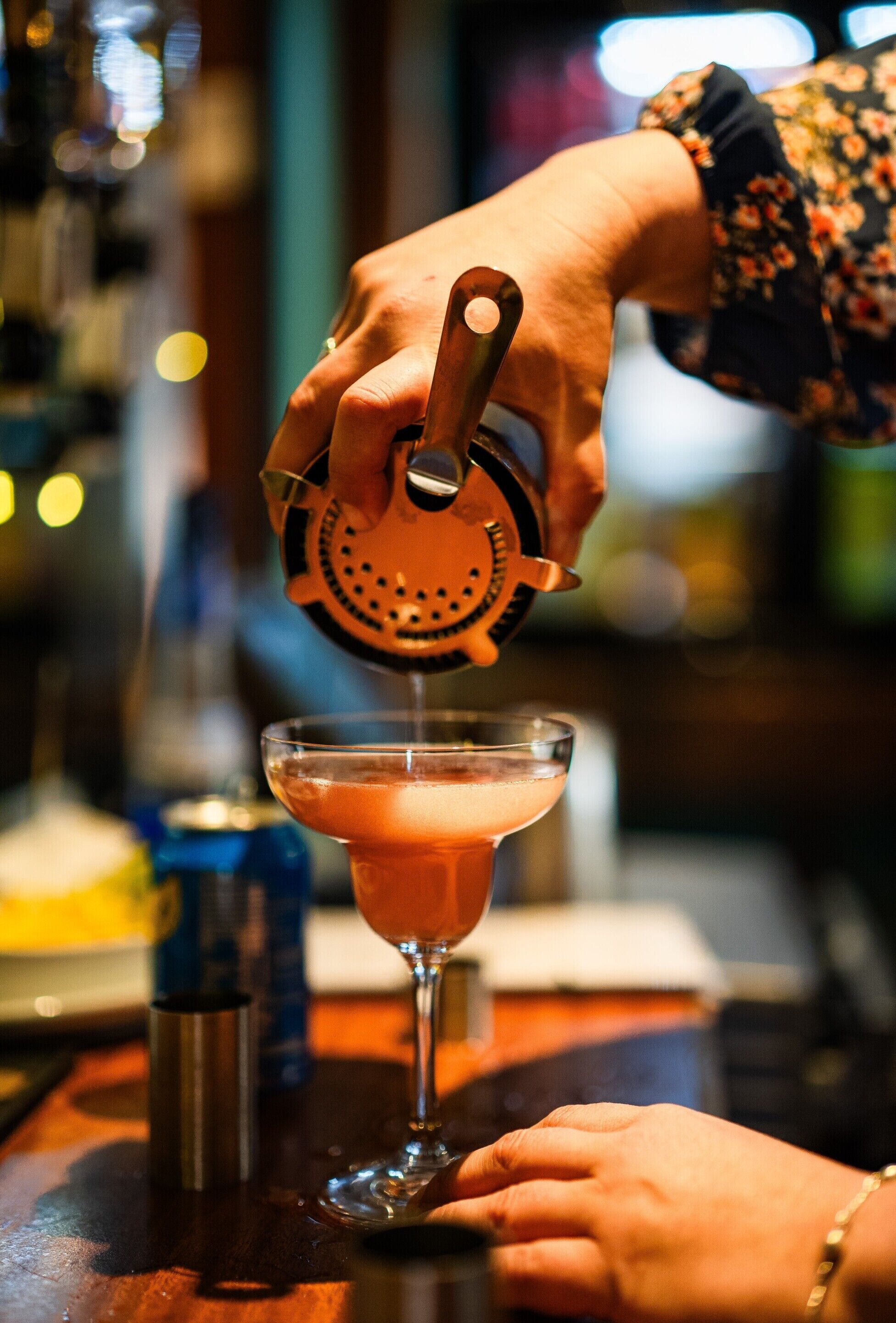 A person using a jigger to measure and pour a drink into a martini glass.