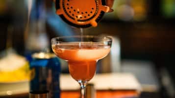A person using a jigger to measure and pour a drink into a martini glass.