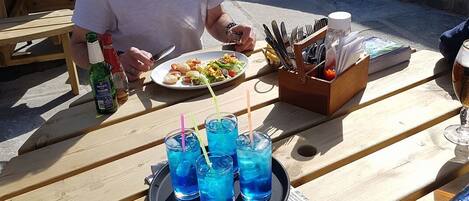 Una mesa de madera con un plato de comida, una botella de cerveza y una bandeja de bebidas azules.