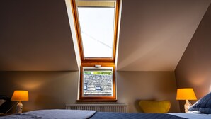 A bedroom with a skylight, two bedside lamps, a radiator, and a yellow pillow.