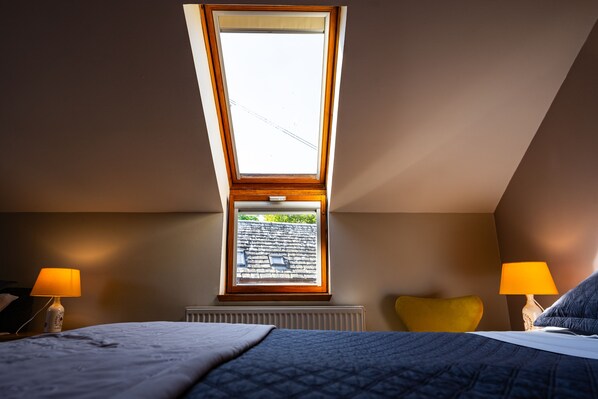 A bedroom with a skylight, two bedside lamps, a radiator, and a yellow pillow. - Murray Arms Hotel (South Ronaldsay)