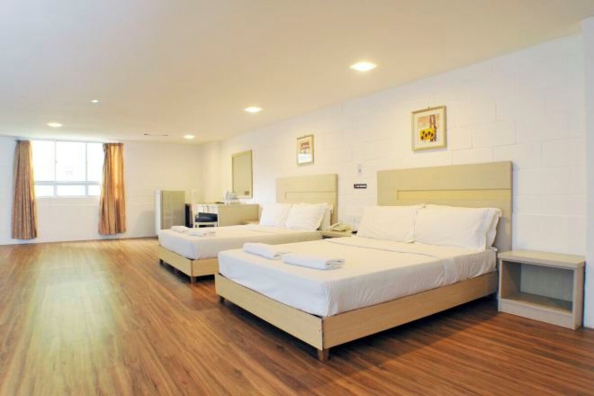 A hotel room with two beds, wooden flooring, white walls, and a small bedside table.