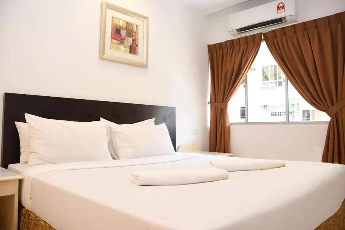 Une chambre d’hôtel avec un grand lit, du linge de lit blanc, une tête de lit noire, un tableau encadré au mur, des rideaux marron et un appareil de climatisation.