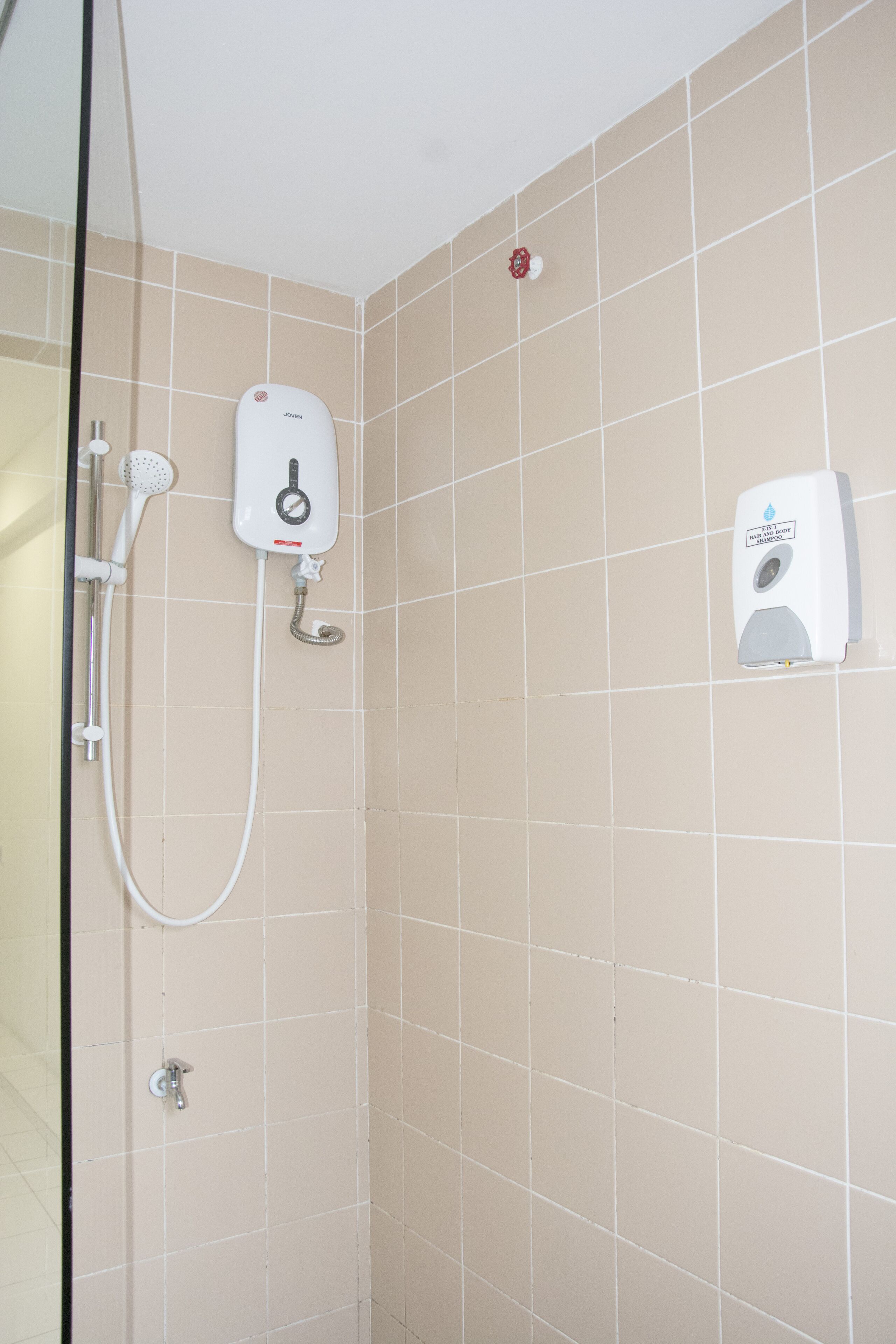 A bathroom with beige tiles, a glass shower enclosure, a handheld showerhead, a wall-mounted hand dryer, and a soap dispenser.