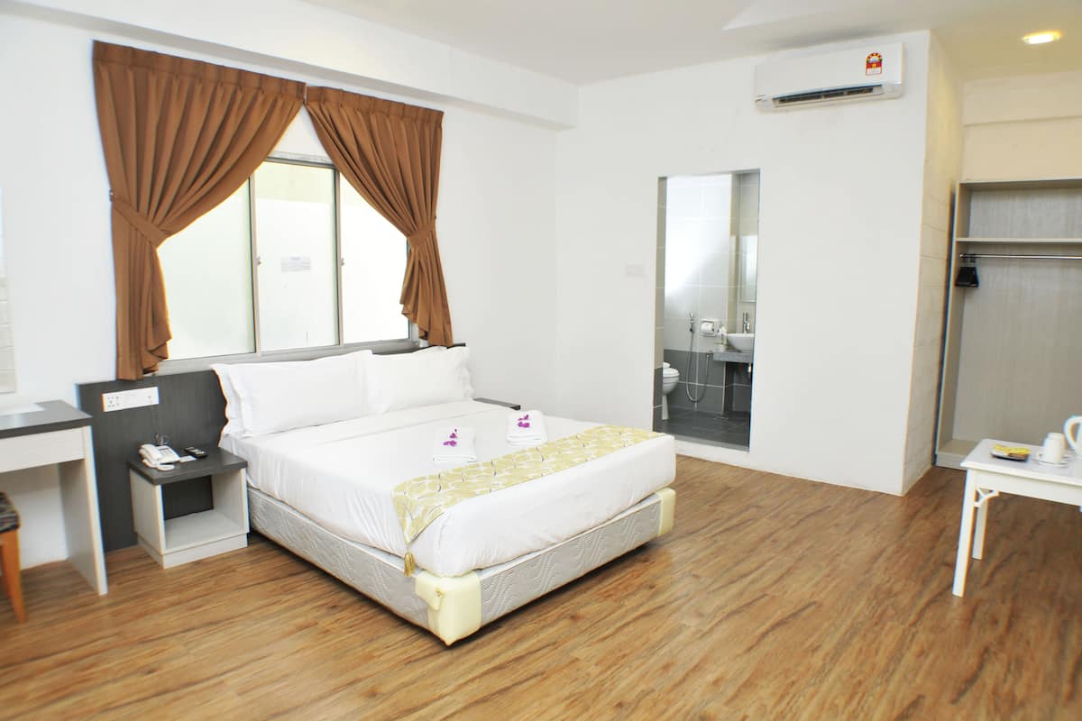 Une chambre d’hôtel comprenant un lit, un bureau, une table de chevet, une salle de bain avec un miroir et un appareil de climatisation.