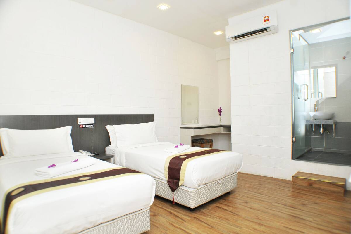 Une chambre d’hôtel avec deux lits, une salle de bain avec une douche en verre et un petit coin salon.