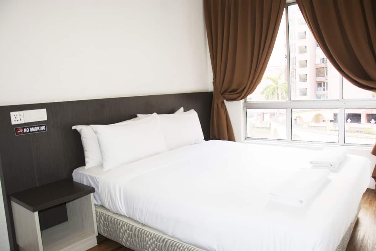 Une chambre d’hôtel avec un lit, une table de chevet, un panneau « Il est interdit de fumer » et une fenêtre avec des rideaux.