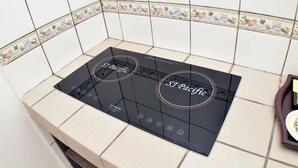 A kitchen with a black induction cooktop and a tiled backsplash. - Promenade Service Apartments (Kota Kinabalu)