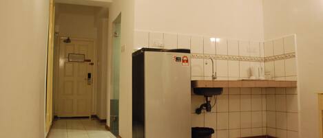 Una pequeña cocina con refrigerador, pileta y salpicadero de azulejos.