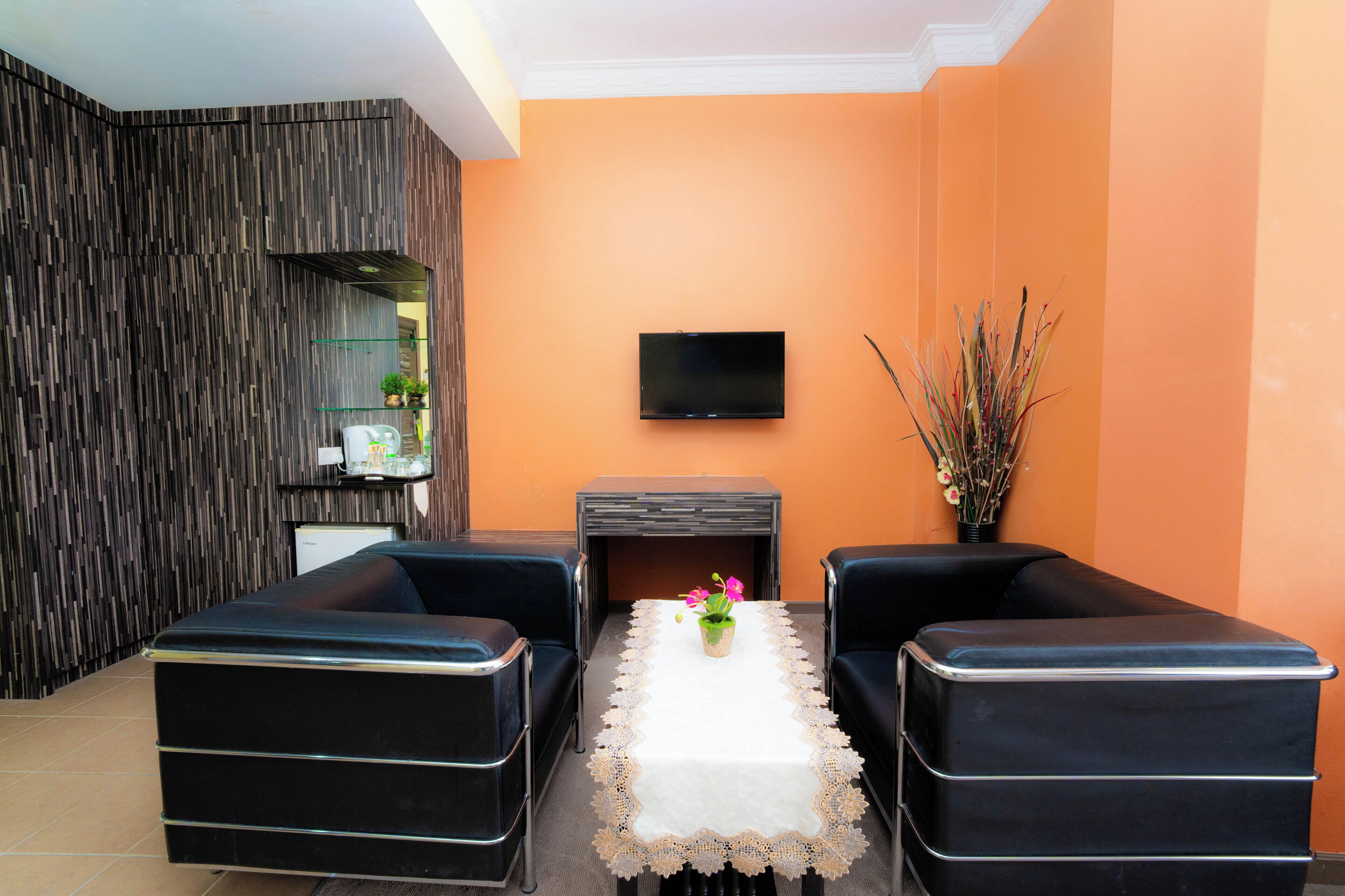 Un salon moderne avec une cheminée, deux canapés en cuir noir, un téléviseur fixé au mur et une plante en pot sur la table.