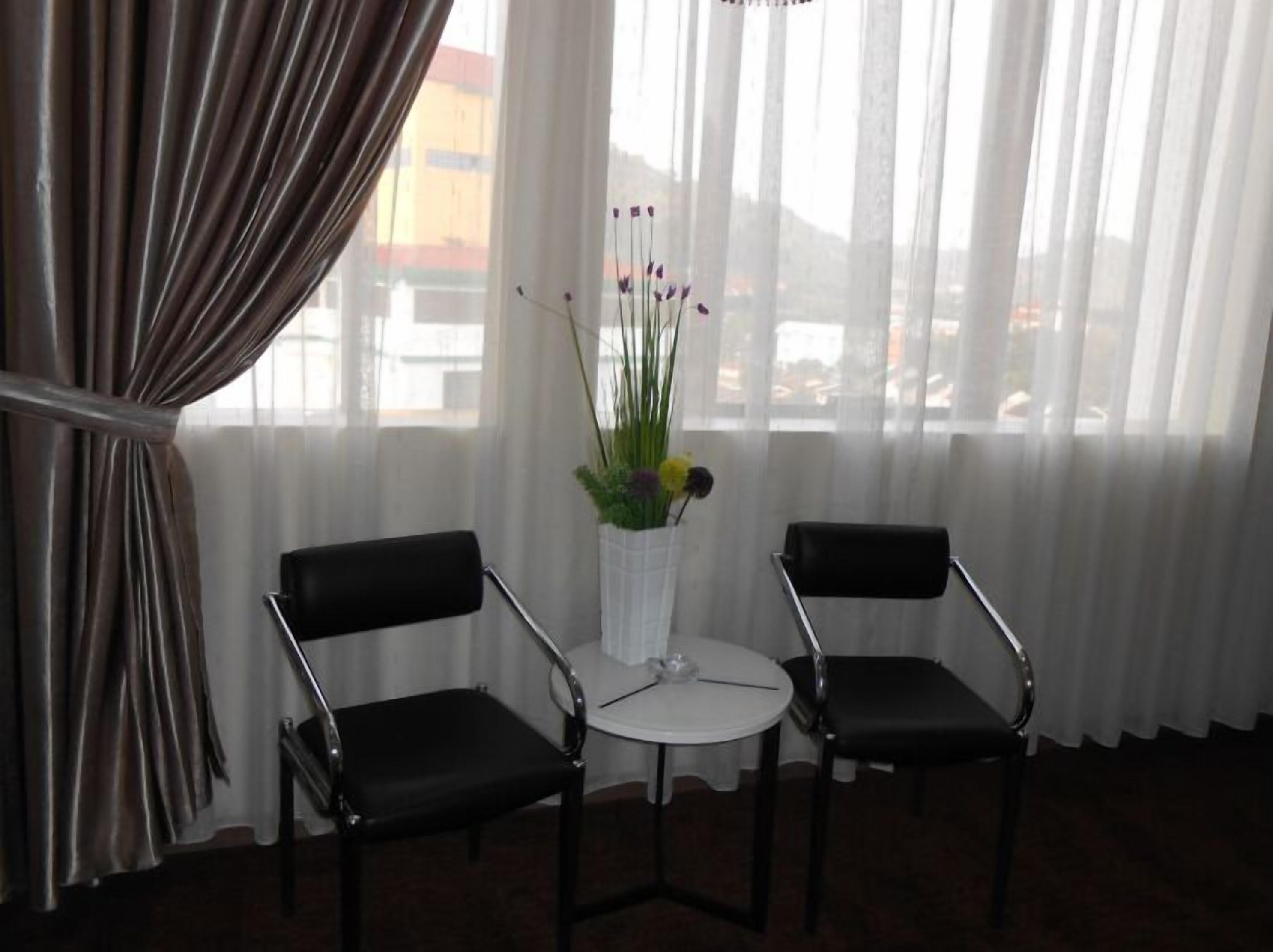 A room with two black chairs, a small round table, and a potted plant with flowers.