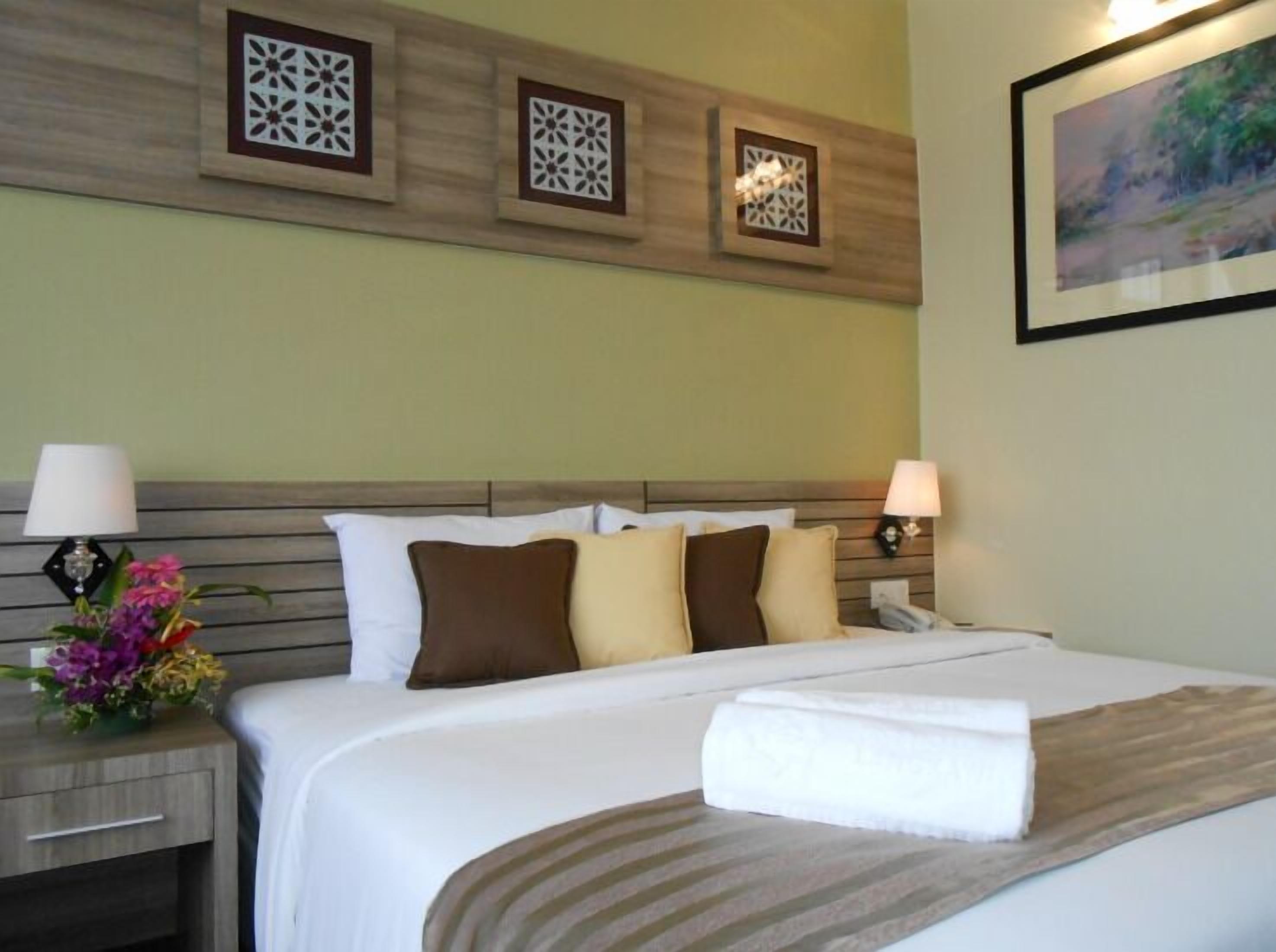 A hotel room with a bed, nightstands, lamps, decorative wall panels, and a framed picture.