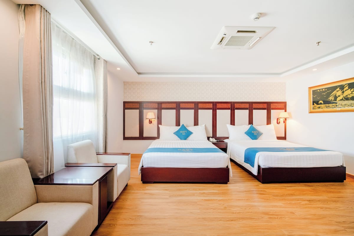 A hotel room with two beds, a sofa, a desk, and a large window with curtains.