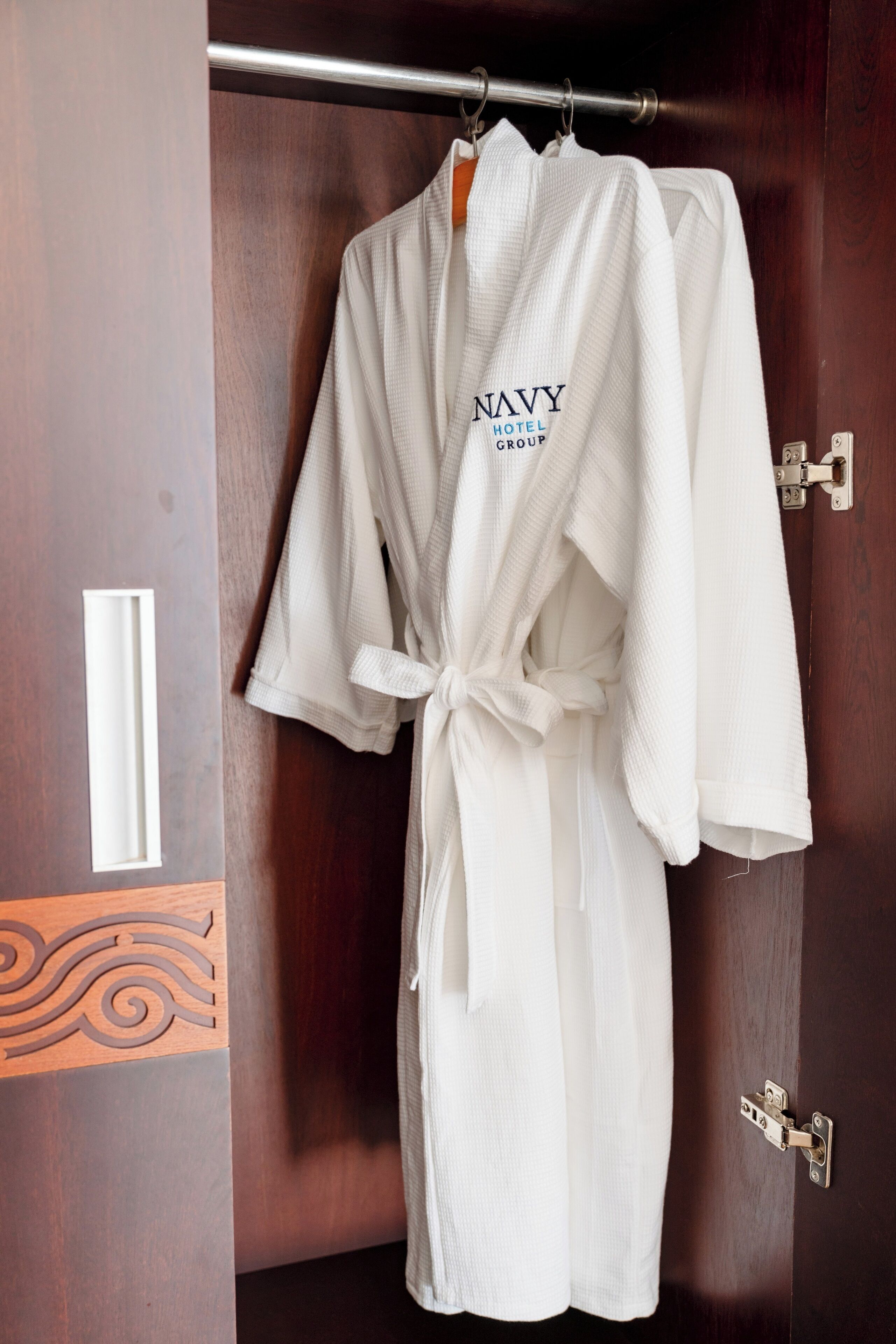 A white robe with "Navy Hotel Group" text hanging on a door.