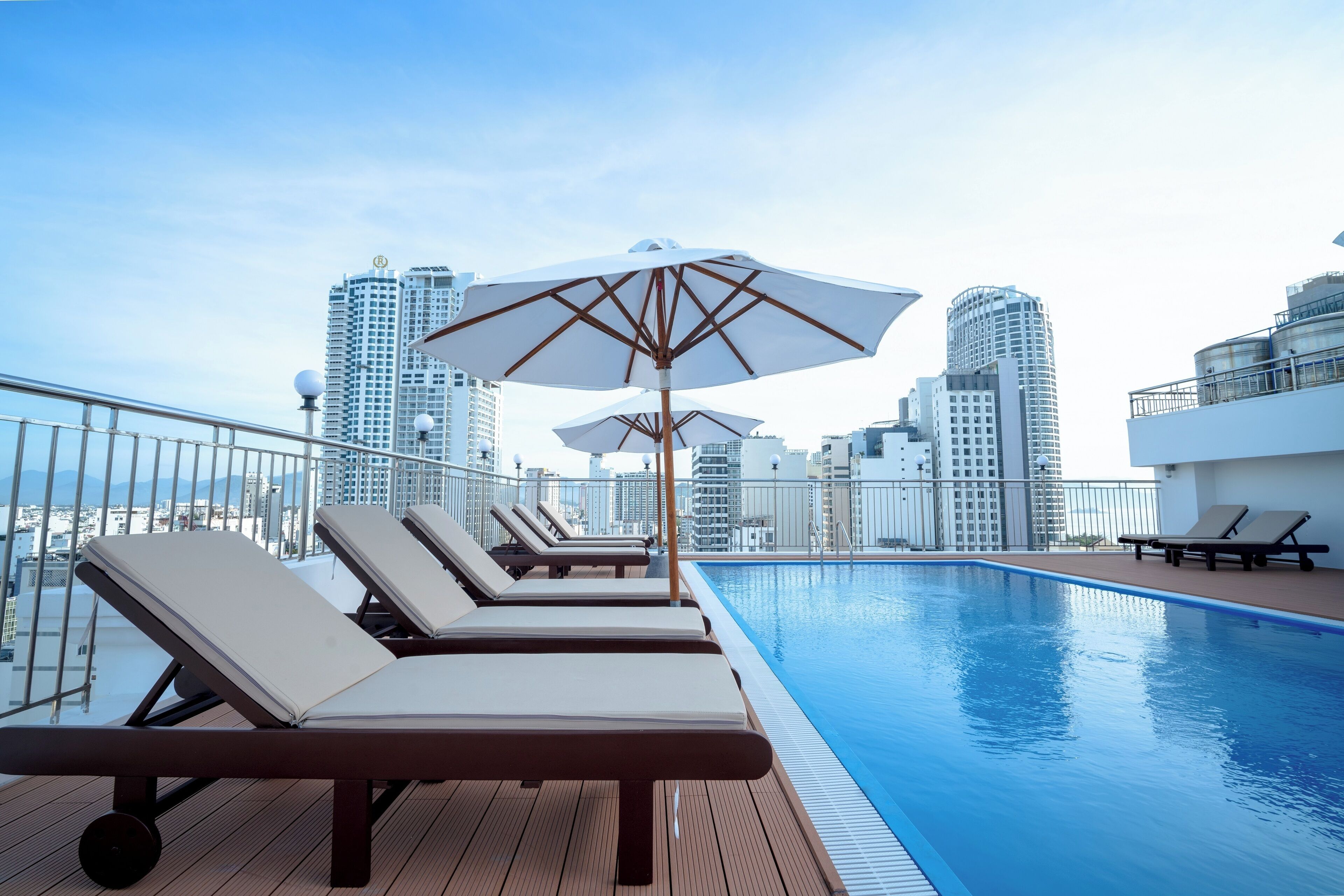 A rooftop pool area with lounge chairs and umbrellas, surrounded by high-rise buildings.