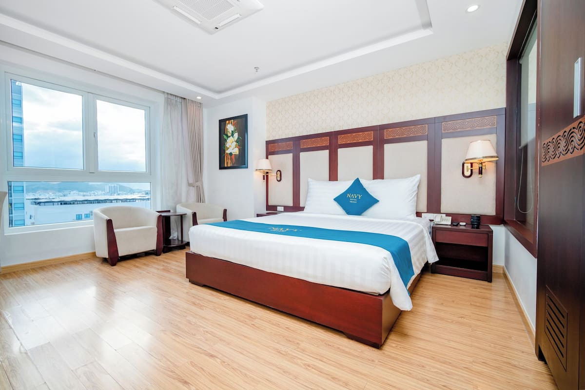 A hotel room with a large bed, a chair, a desk, and a view of the city.