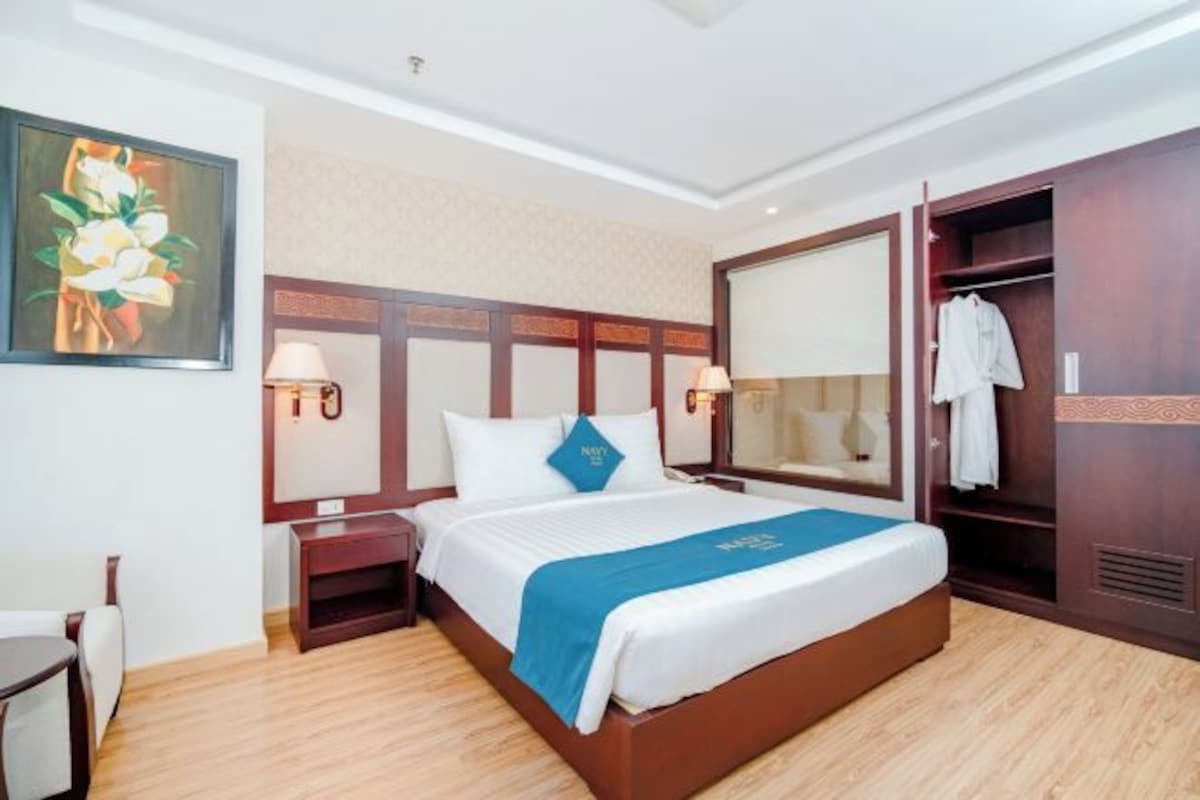 Una habitación de hotel con una cama grande, un armario, una mesita de noche con lámpara y un cuadro en la pared.