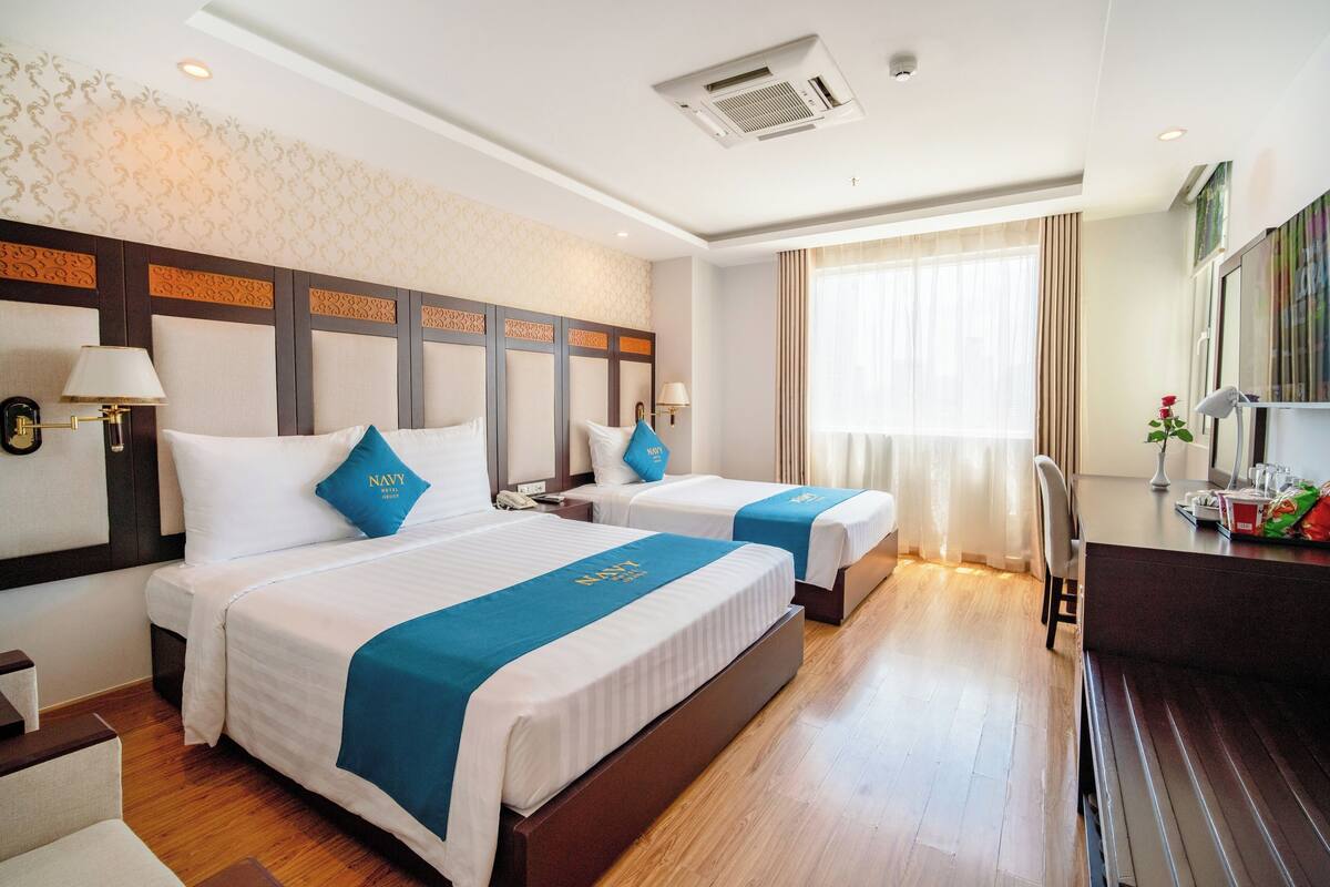 A hotel room with two beds, a desk, a chair, and a large window with curtains.