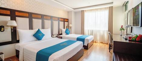 Habitación de hotel con dos camas, un escritorio, una silla y un ventanal con cortinas.