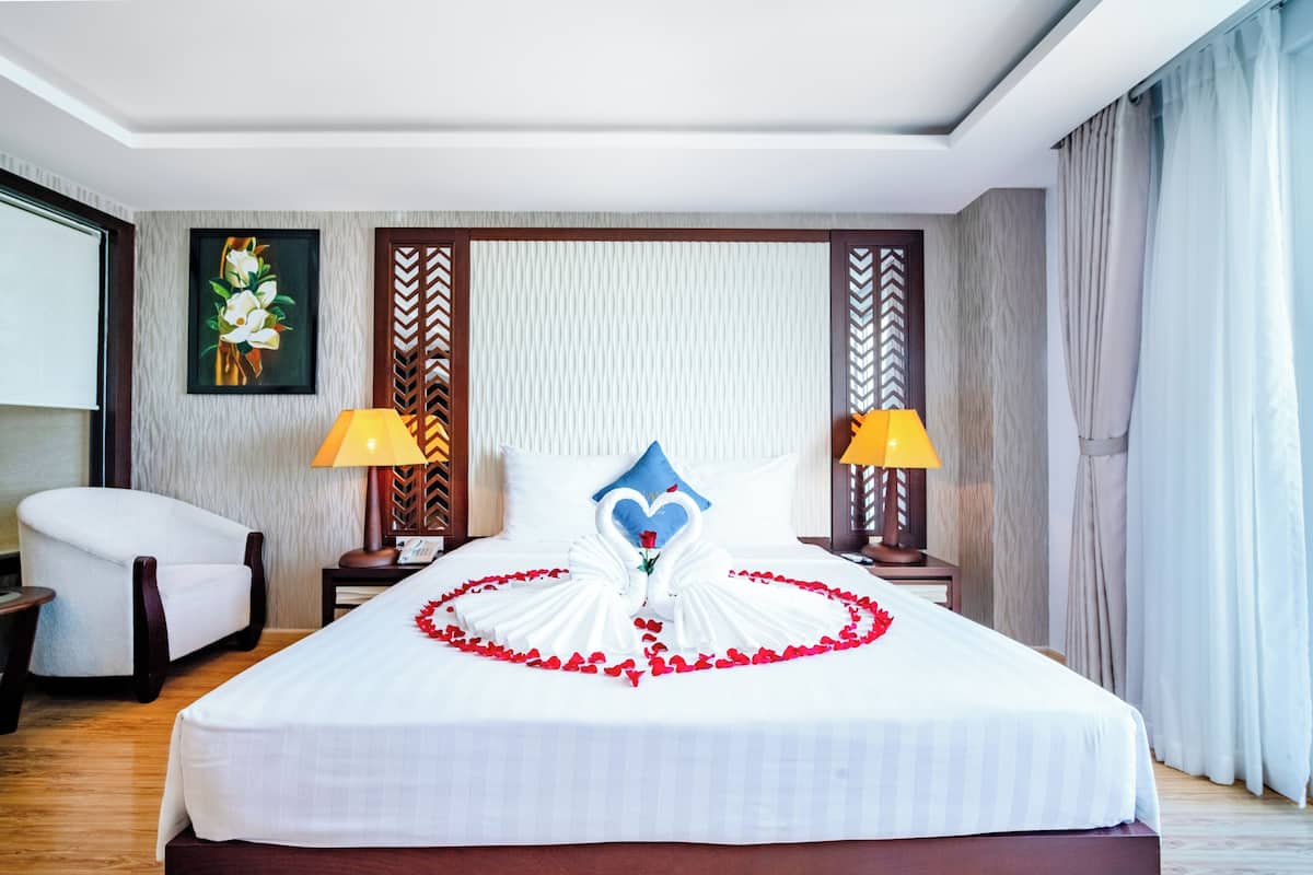 A neatly made bed with a heart-shaped decoration of red petals and a blue pillow.