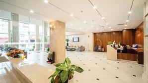 A hotel lobby with a reception desk, seating area, and large windows. - Galliot Hotel Nha Trang (Nha Trang)