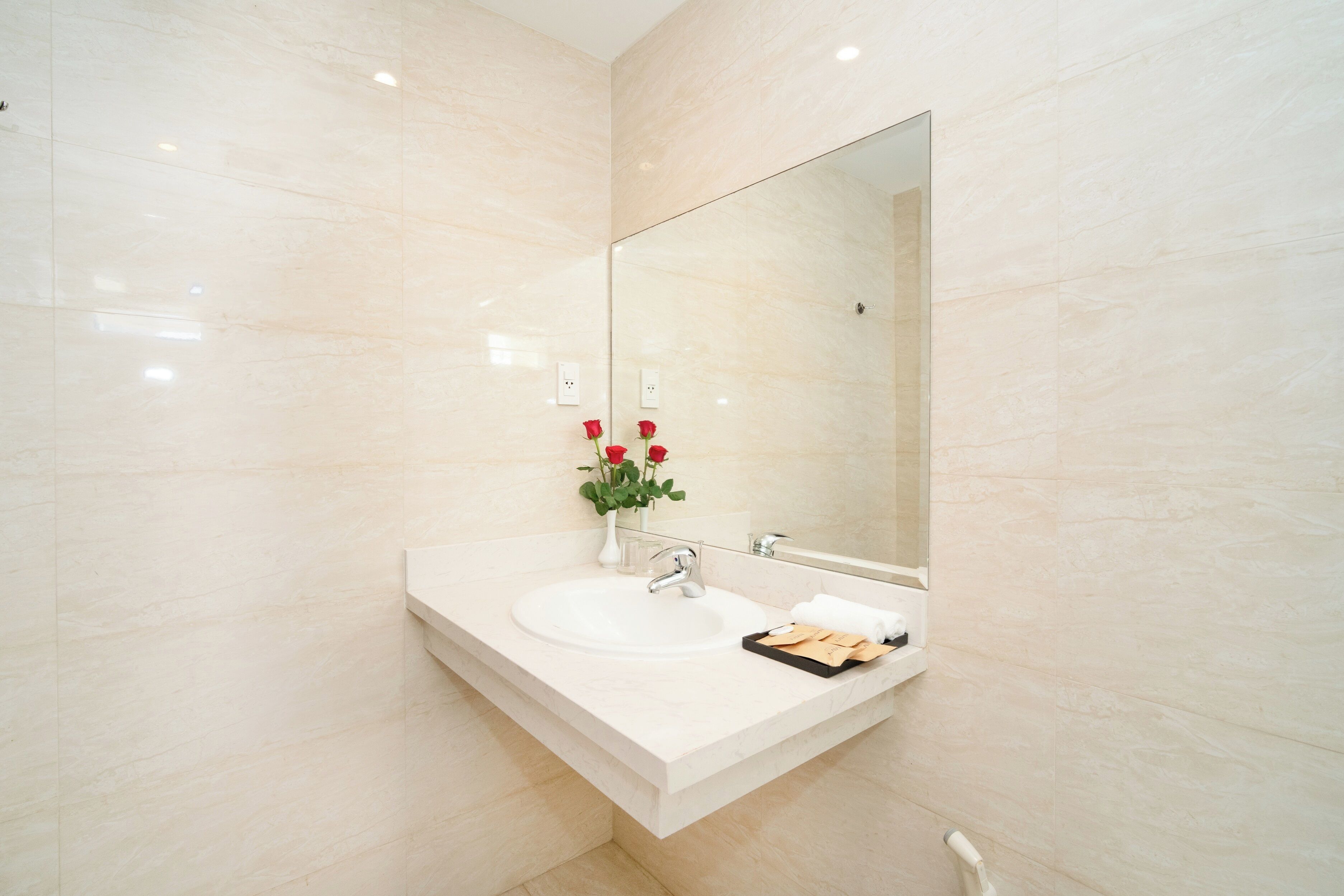 A modern bathroom with a white sink, a large mirror, and a vase with red flowers.