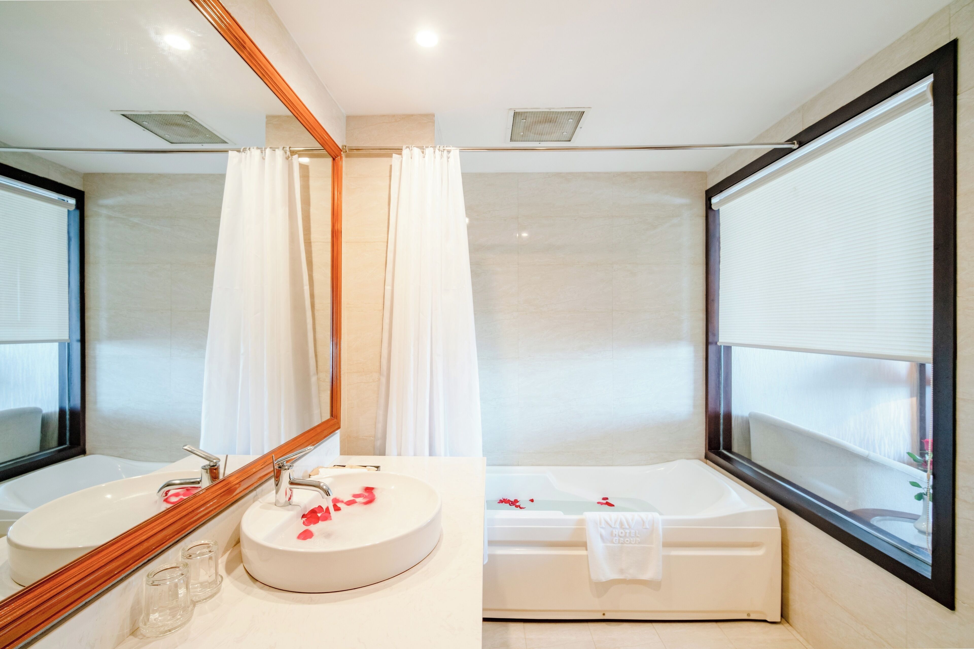 Un baño moderno con un espejo grande, dos lavamanos, una bañera y una ventana con persianas.