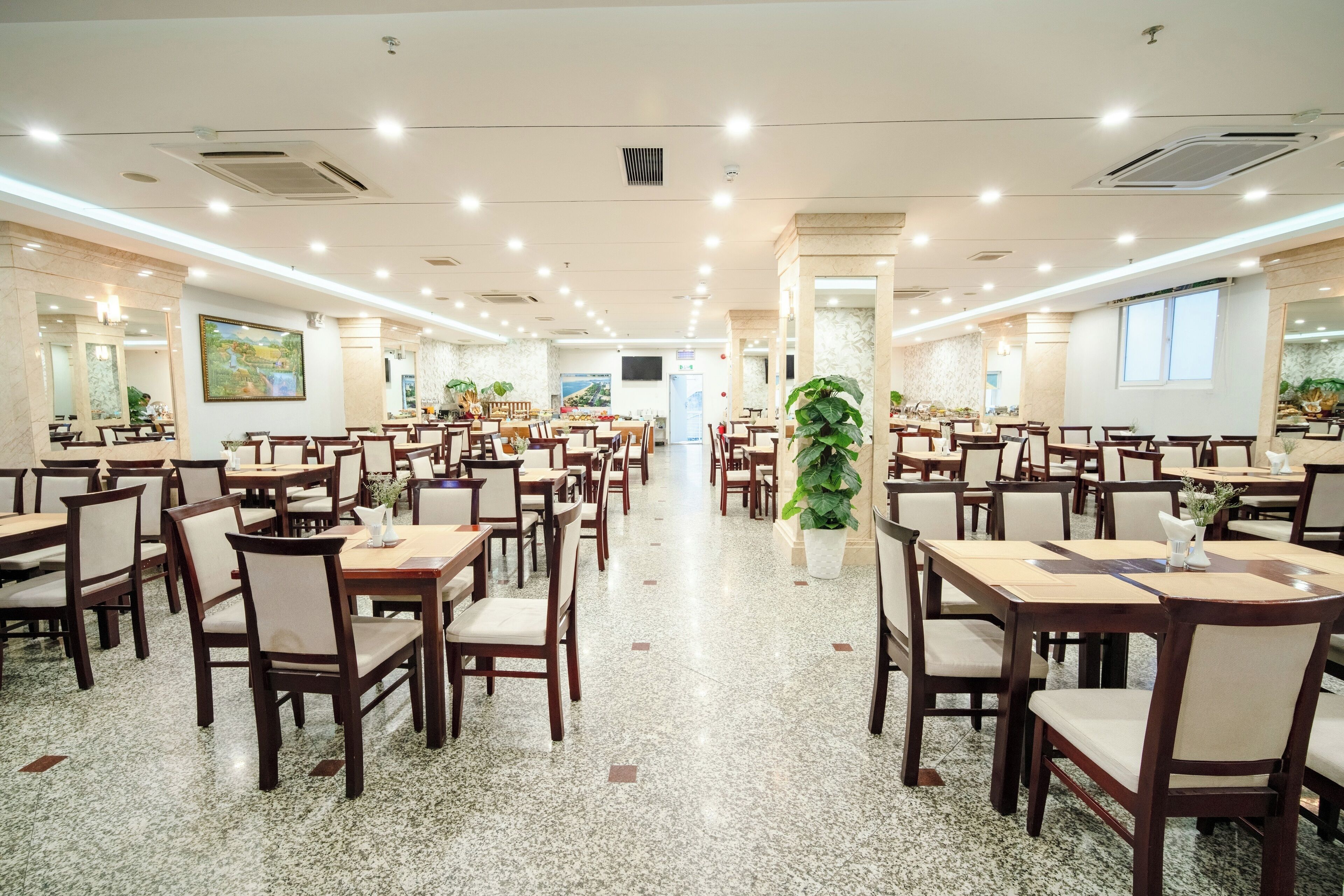 A spacious dining area with multiple tables and chairs, a polished granite floor, and a central pillar with a plant.