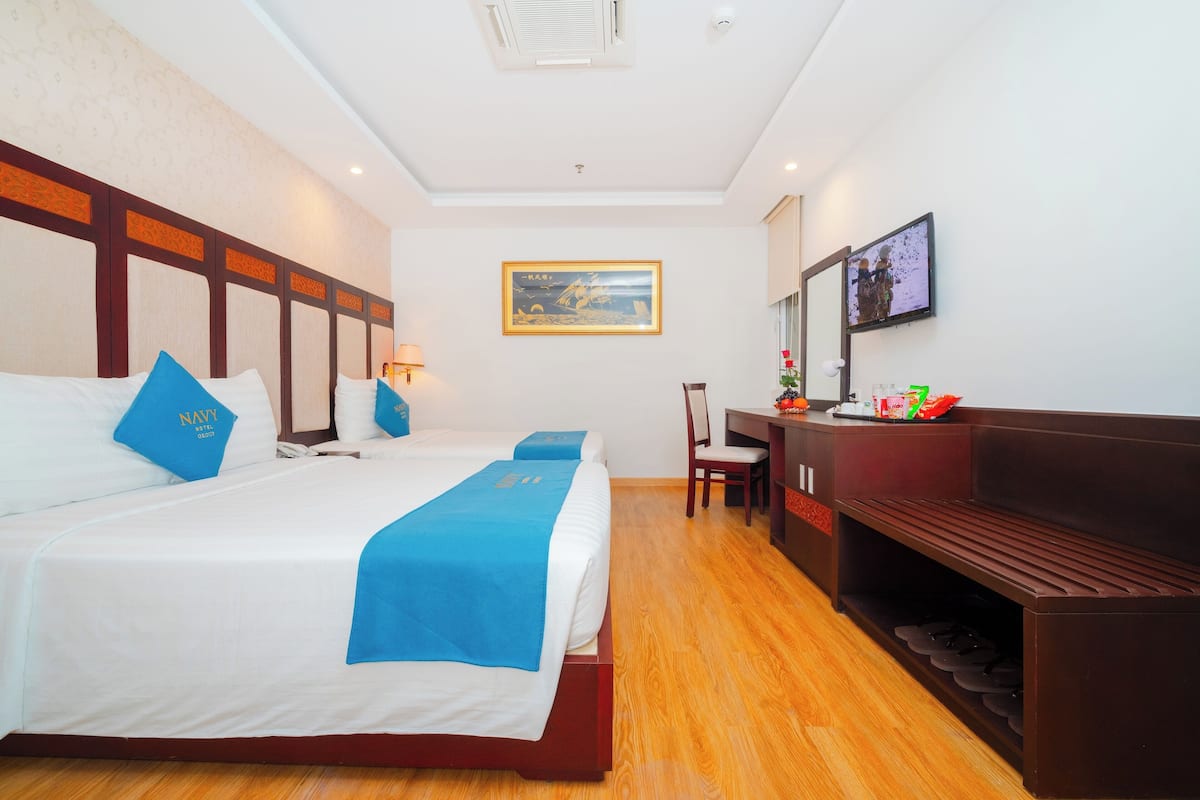 A hotel room with two beds, a desk, a chair, a TV, and a shoe rack.