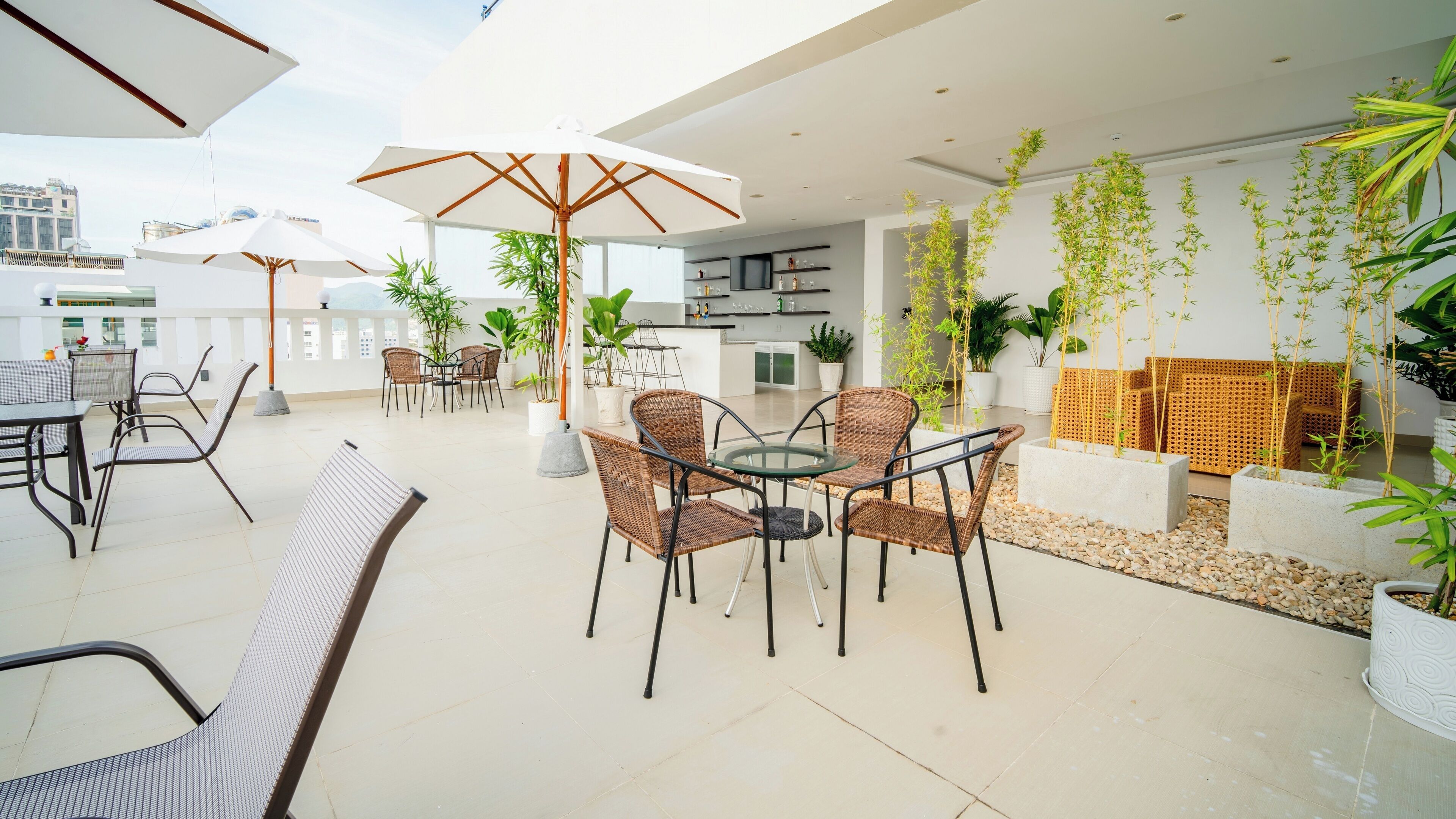An outdoor patio area with wicker furniture, a glass table, and potted plants.