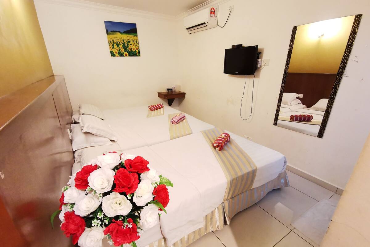 A hotel room with a bed, a bedside table, a mirror, a wall-mounted TV, and a painting.