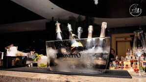 A bar area with a marble countertop, a glass container holding multiple bottles, and a bottle of champagne.