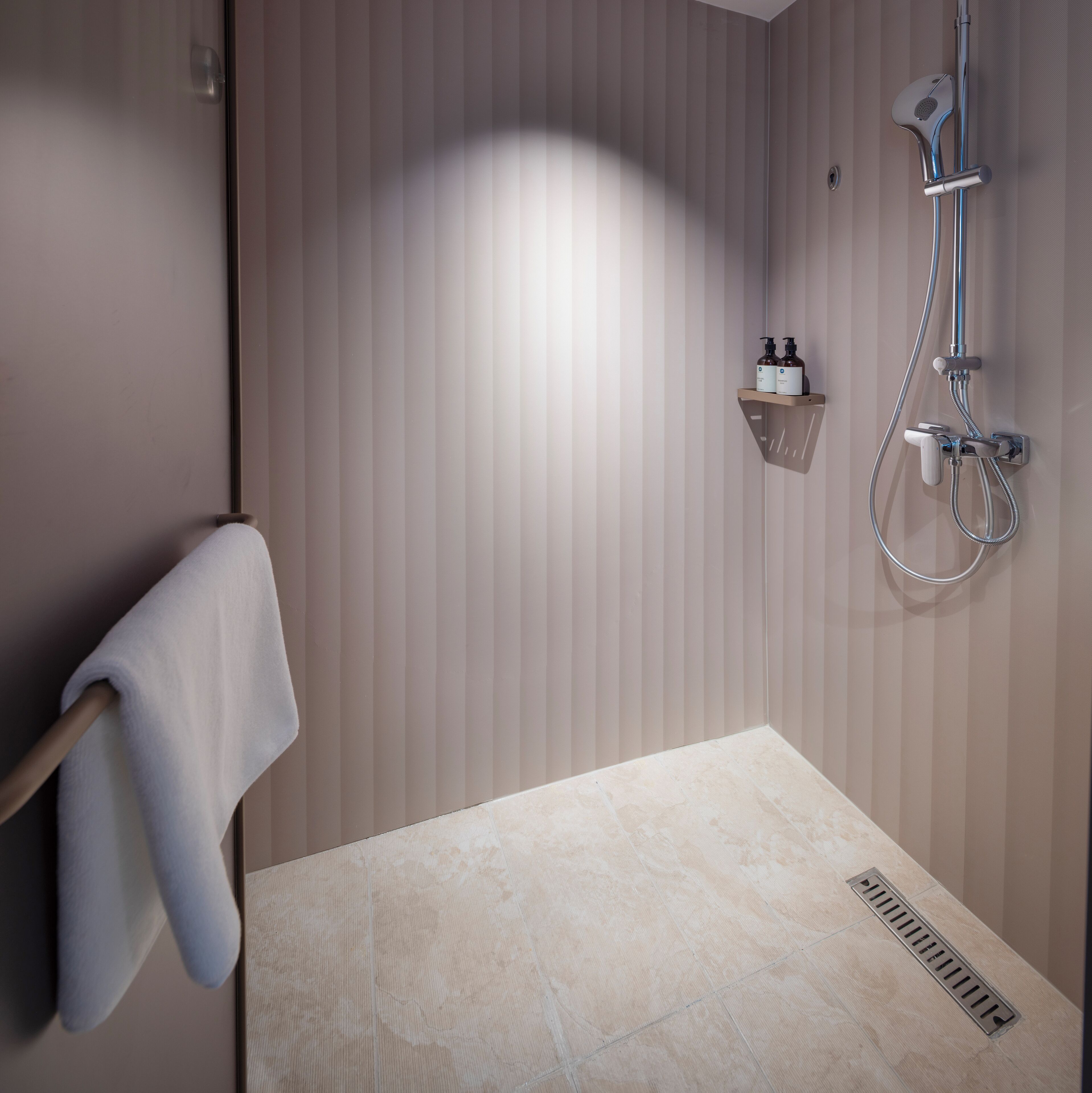 A modern bathroom with a shower, a towel rack, and a shelf with toiletries.