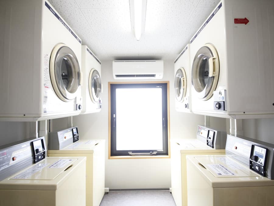 A laundry room with two washing machines, a dryer, and a window.