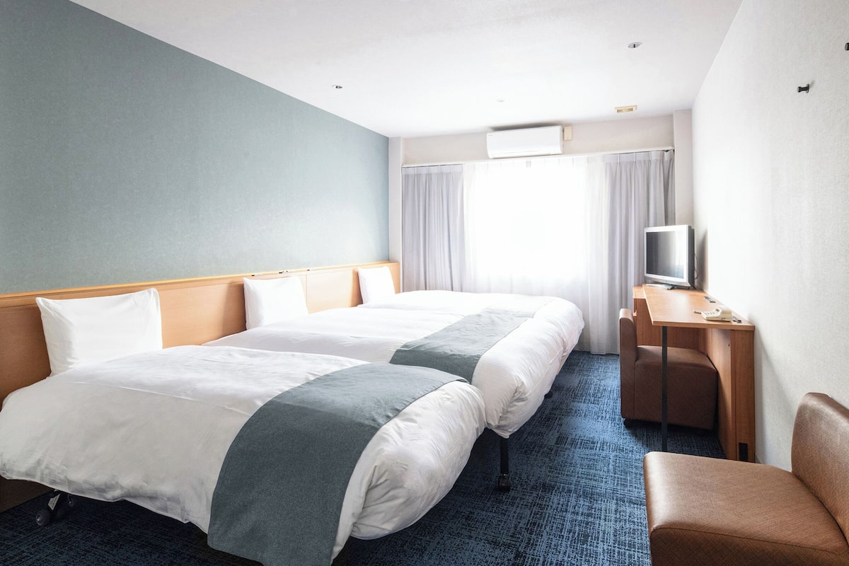 A hotel room with two beds, a desk with a TV, and a chair.