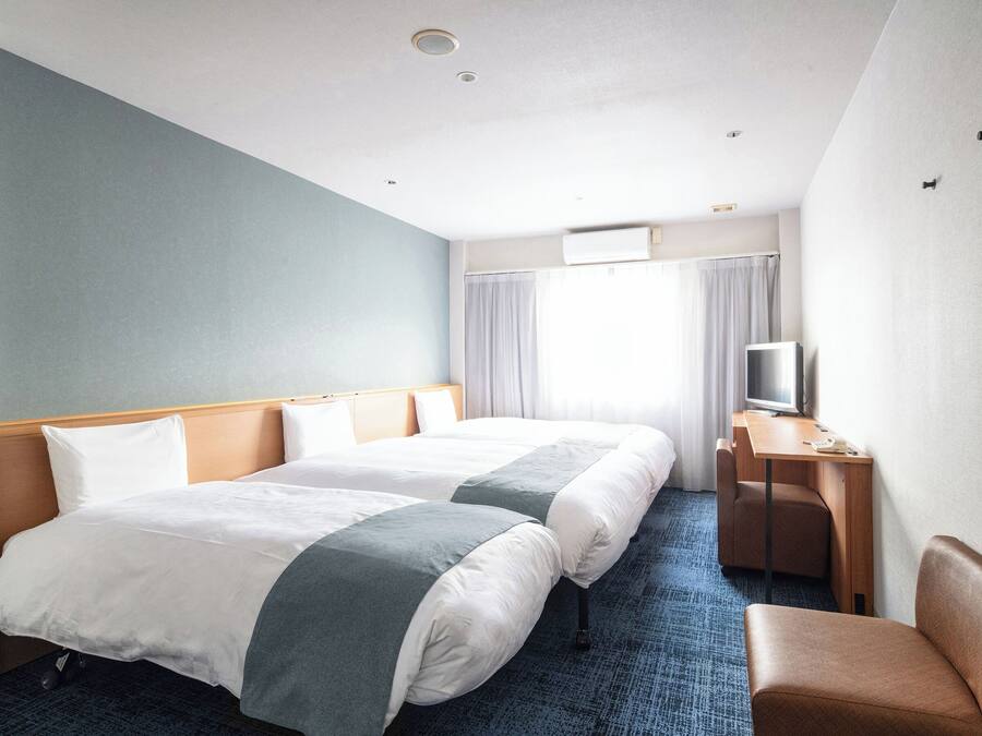 Una habitación de hotel con dos camas, un escritorio con televisor y una silla.