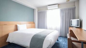 A hotel room with a bed, a desk, a television, and an air conditioning unit.