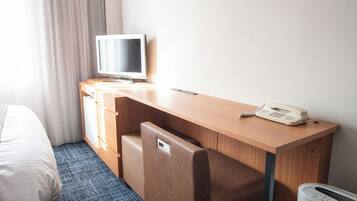 A hotel room with a bed, a desk with a telephone, a television, and a small heater.