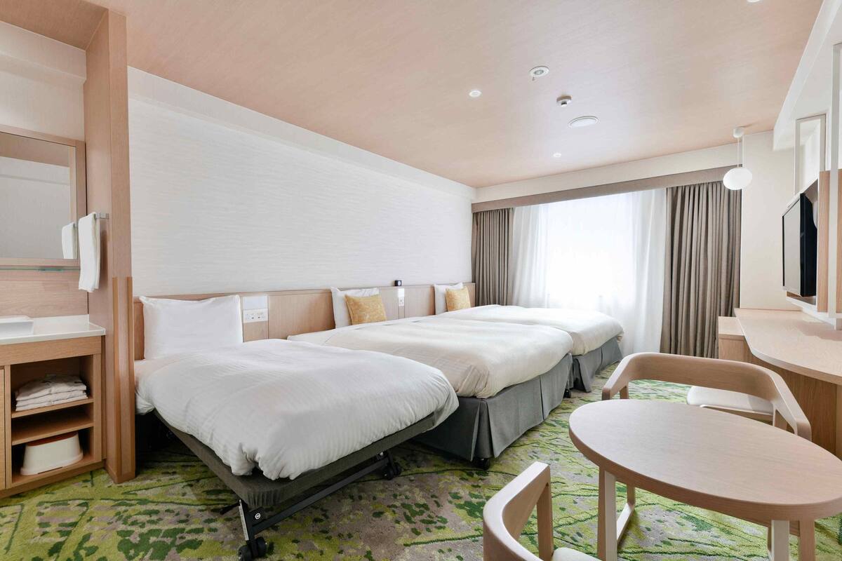 Habitación de hotel con dos camas, un escritorio, una silla y un televisor.