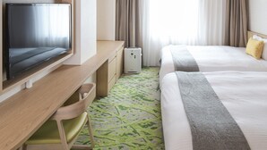Habitación de hotel con televisión de pantalla plana, escritorio, dos camas, un cesto de basura y una ventana con cortinas.