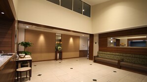 Un lobby moderno de hotel con mostrador de recepción, área de descanso y un espejo grande que refleja el espacio.
