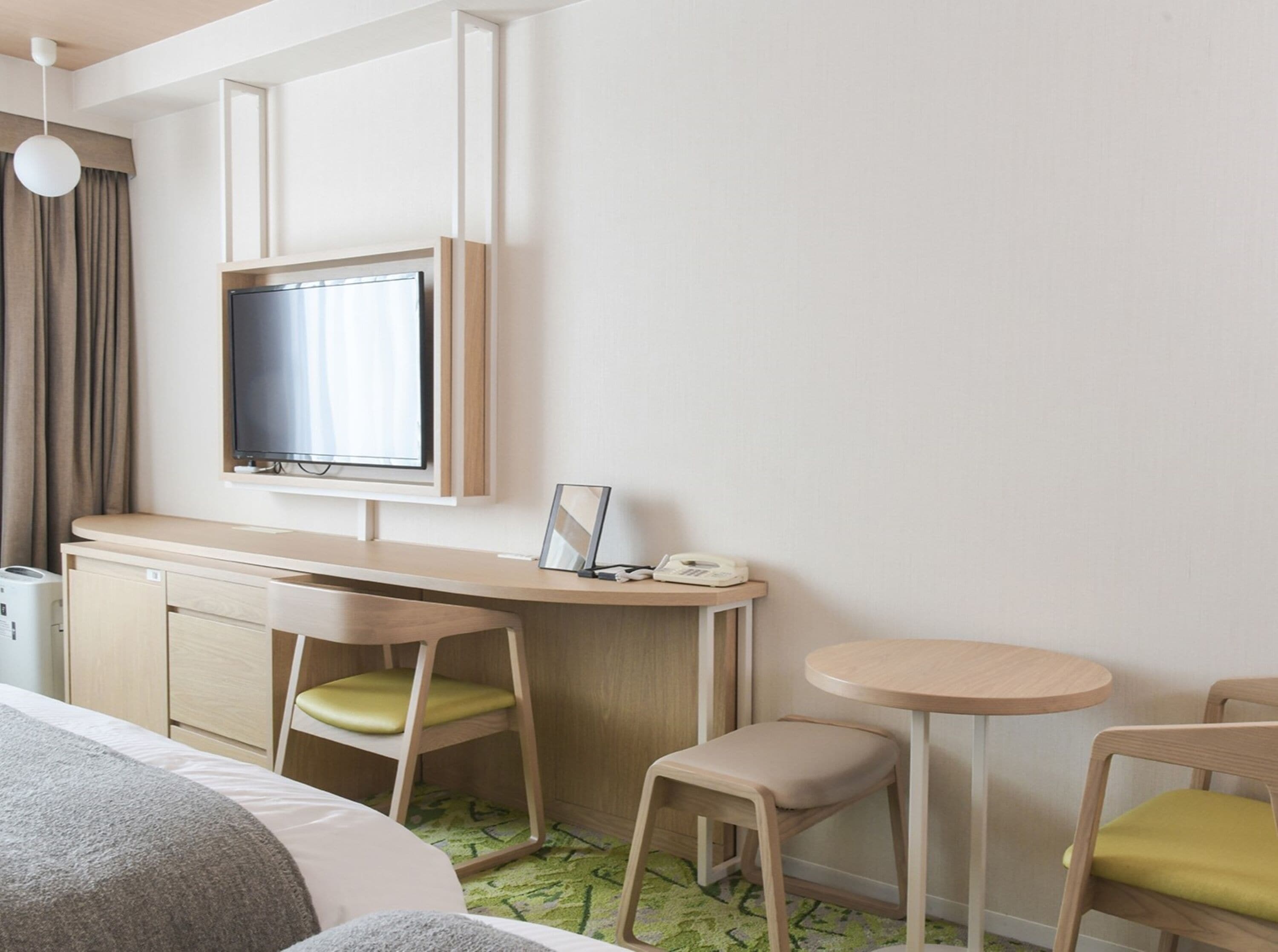A hotel room with a bed, a desk with a chair, a television, and a small table with a chair.