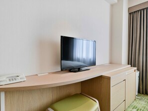 Een hotelkamer met een flatscreen televisie op een houten bureau, een groene stoel en een telefoon.