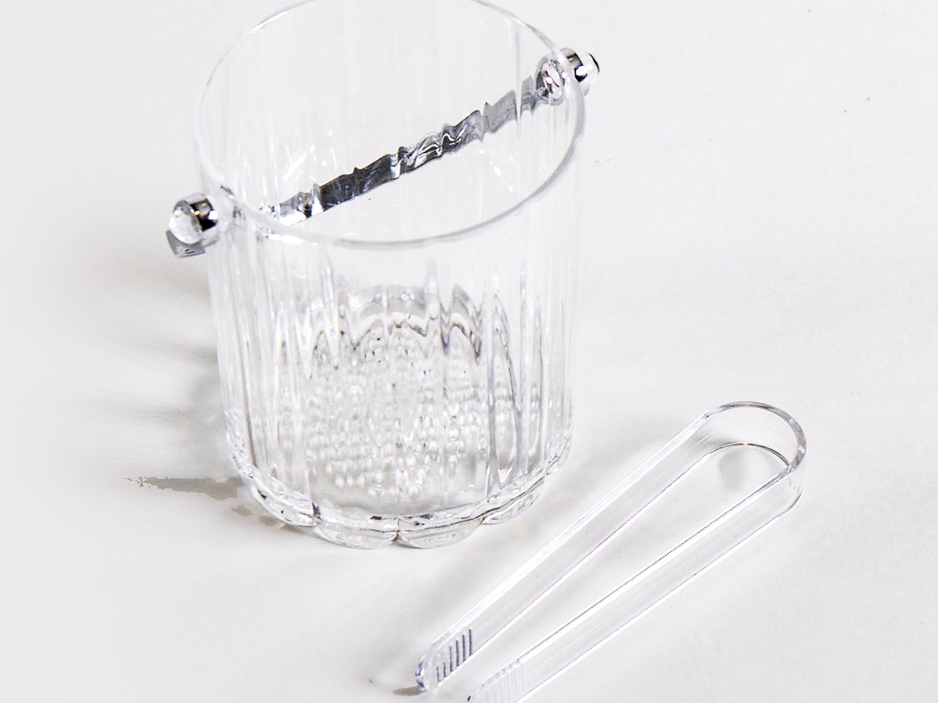 A clear glass mug with a handle and a metal clasp, accompanied by a clear plastic spoon.