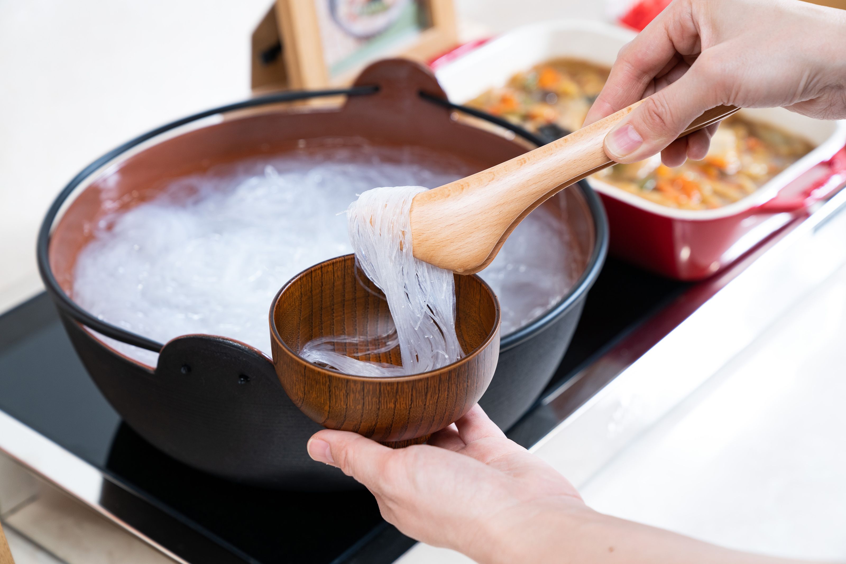 Una persona sirve fideos de una olla a un tazón.