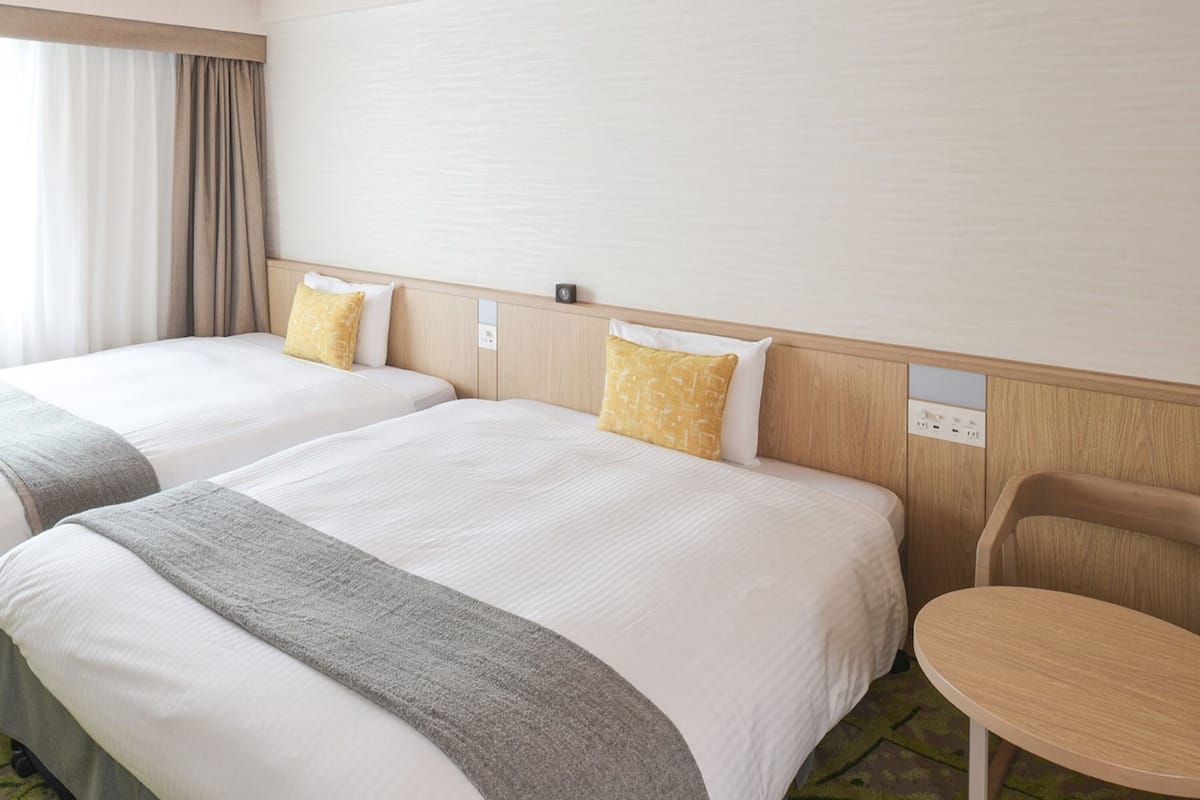 Habitación de hotel con dos camas, una mesita y una ventana con cortinas.